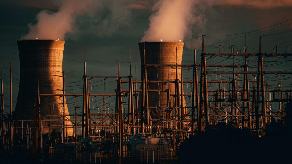 Instalaciones industriales de una planta de generación eléctrica iluminadas durante la noche, con vapor saliendo de sus torres.